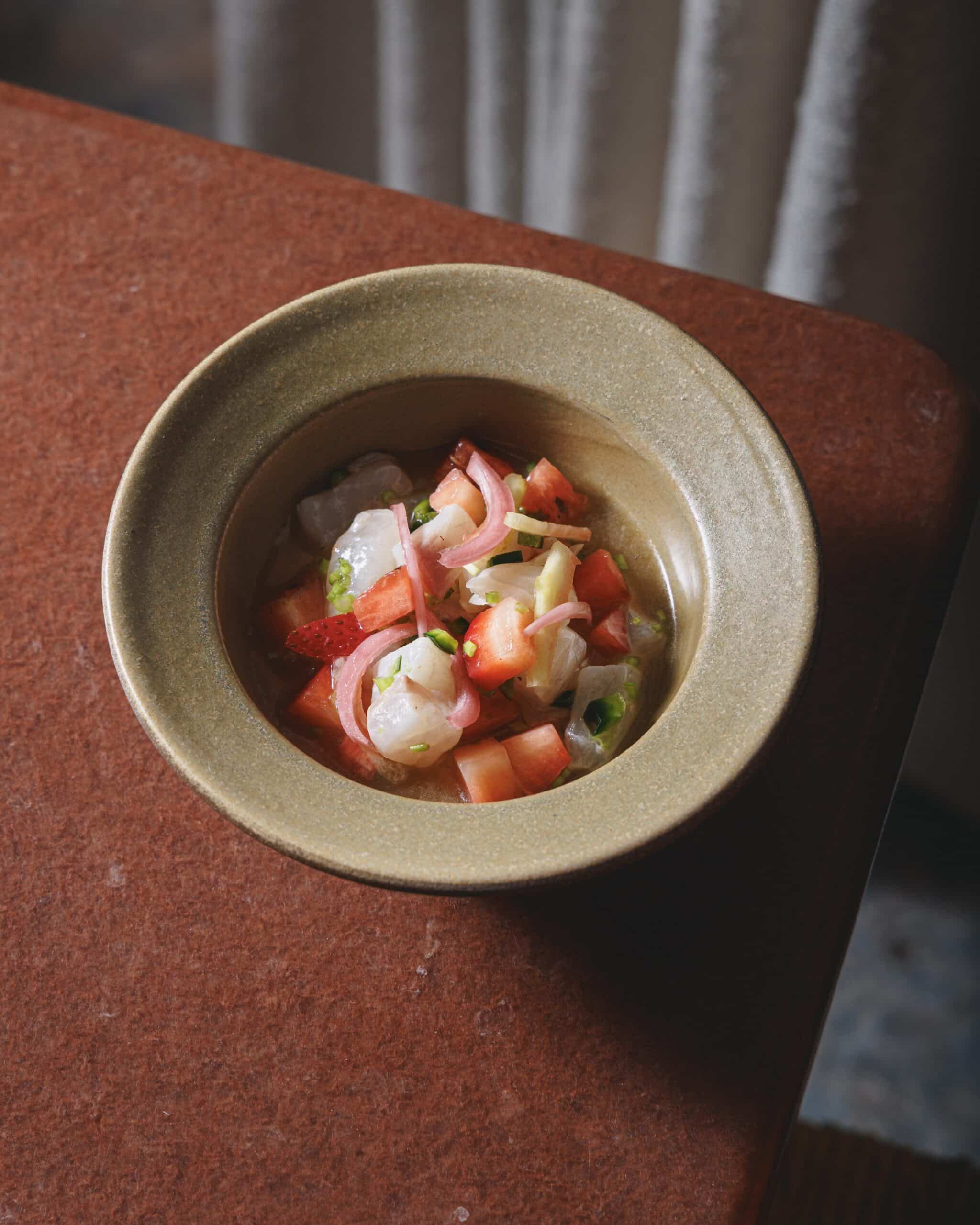 Fresh sea bass ceviche with strawberry, pickled onion, and herbs served in a ceramic bowl at Ara Restaurant in Aldgate East, City of London.