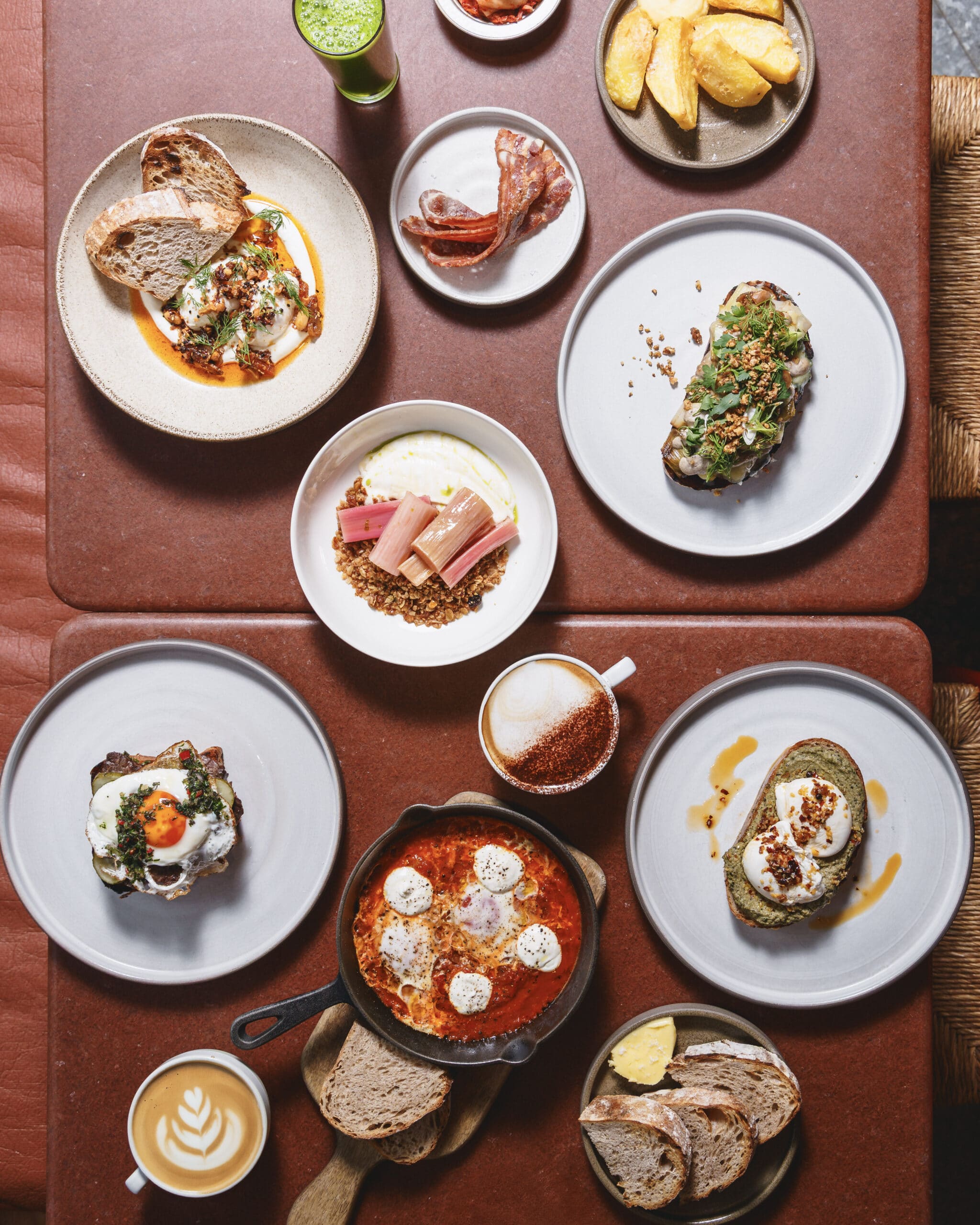 Flat lay of Ara Restaurant’s brunch spread featuring poached eggs with courgette spread, shakshuka, greek yogurt with rhubarb, toast, and monmouth coffee in Aldgate East.