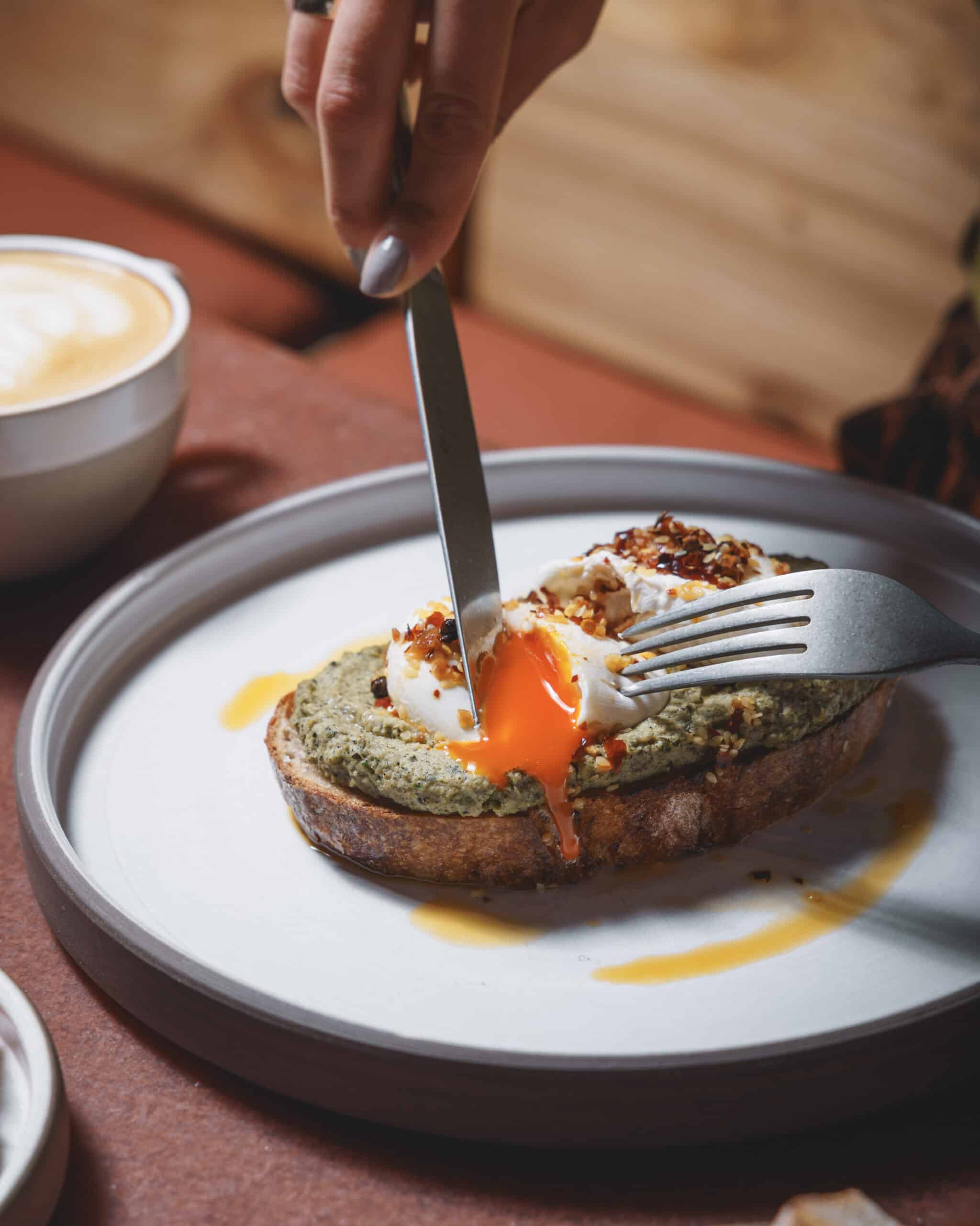 Cutting into poached eggs on courgette spread on toast with chilli oil and feta at Ara Restaurant in Whitechapel, near Spitalfields.