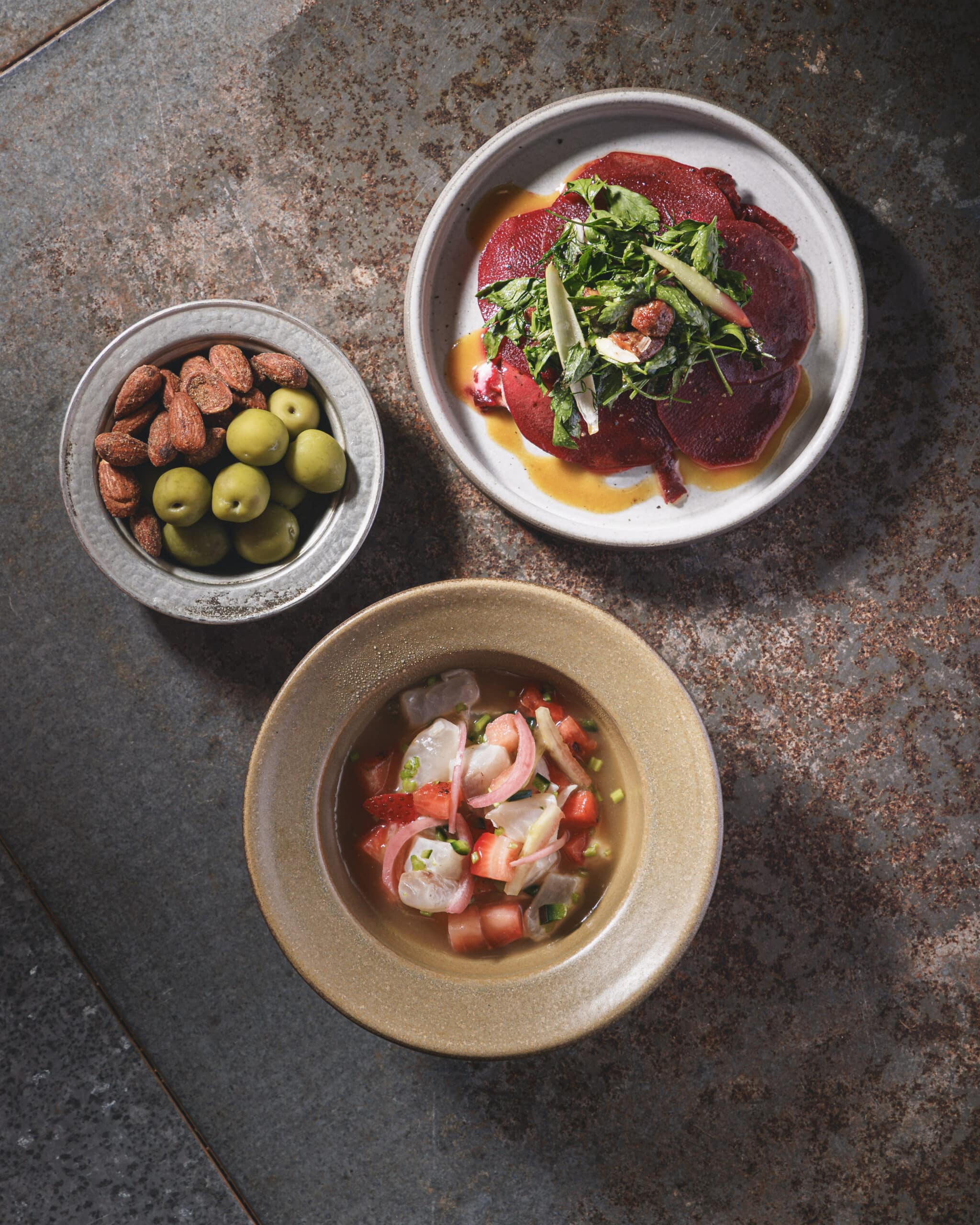 A trio of small plates at Ara Restaurant in Aldgate East, featuring marinated olives with almonds, beetroot carpaccio with greens, and a fresh strawberry ceviche.