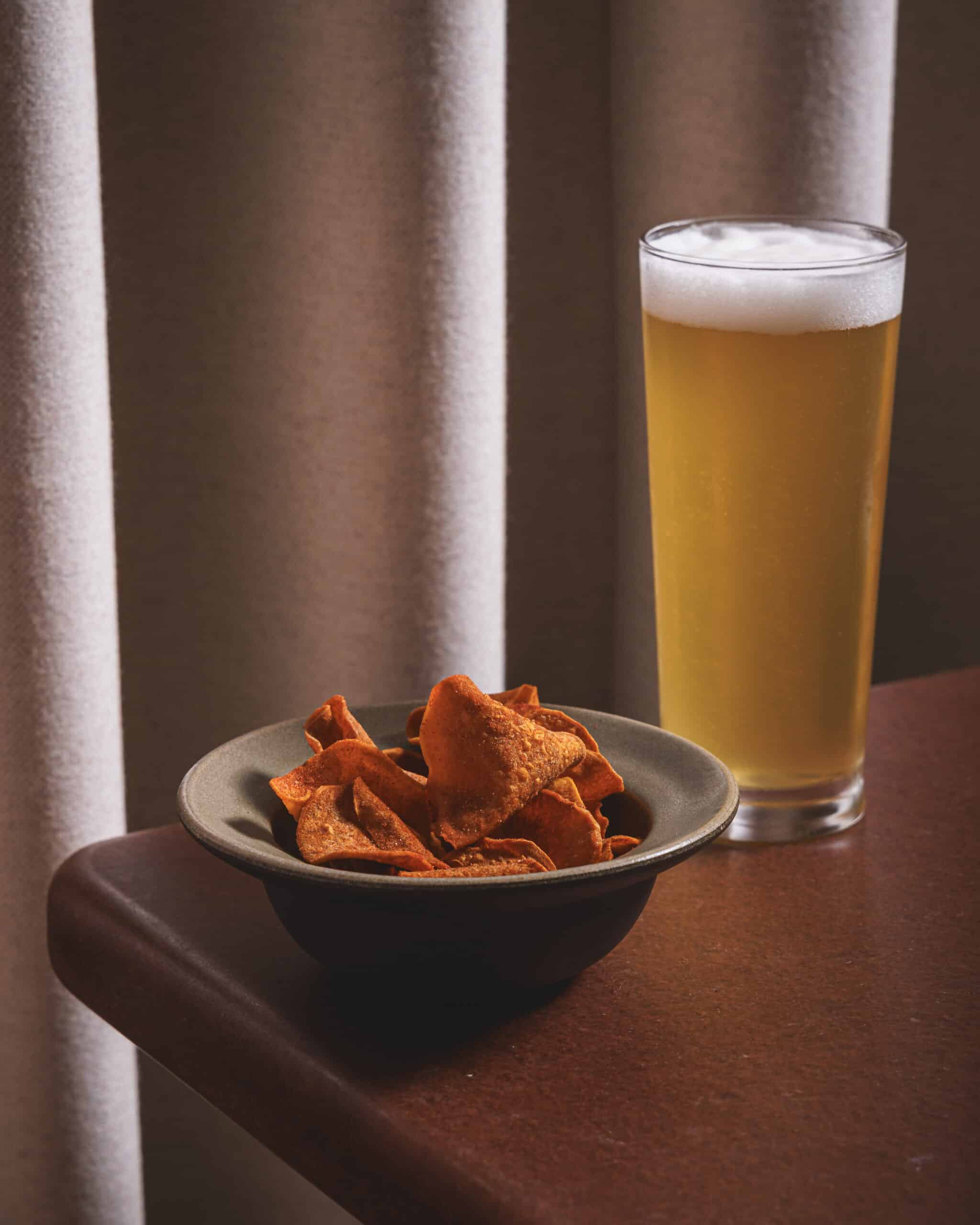 A bowl of spicy sweet potato crisps paired with a cold beer at Ara Restaurant near Aldgate East, London.